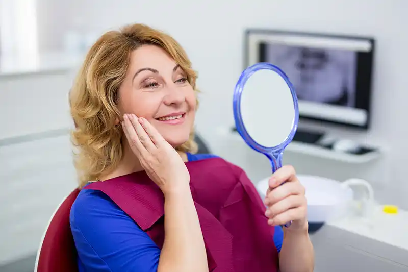 Woman sitting in the dentist chair happily admiring her teeth in a mirror