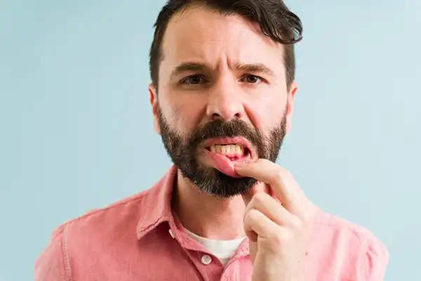 A man pulling down his lip in the mirror to skeptically look at his gums