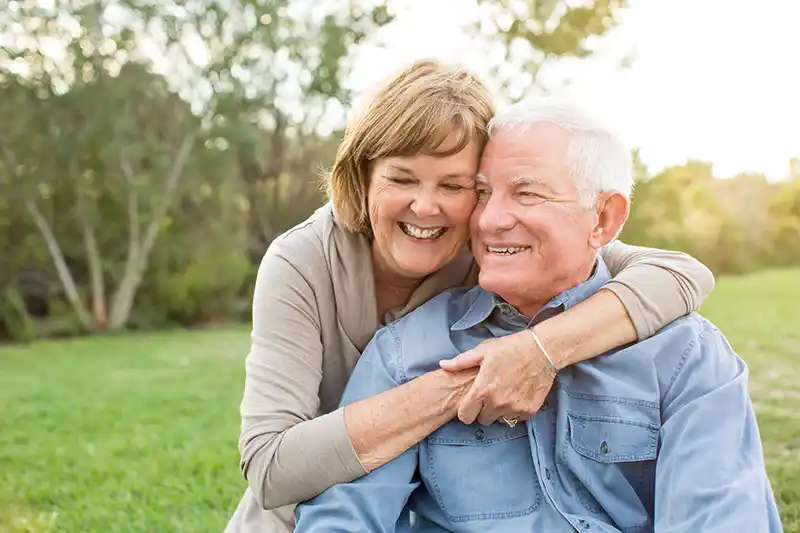 An older couple embracing one another in a park and smiling