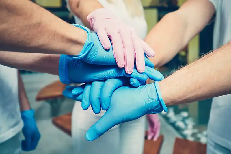 A team of dental professionals putting their gloved hands together to signify dedication and teamwork