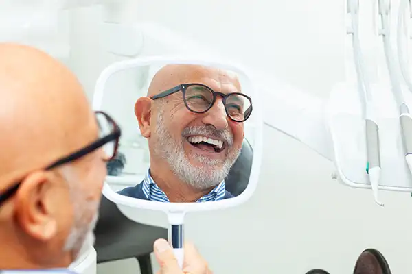 An older man with glasses sitting in the dental chair smiling