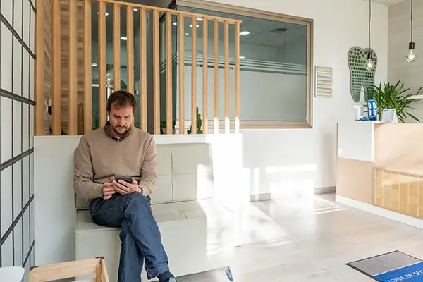 A man looking through his phone in a brightly lit modern office before his dentist appointment.